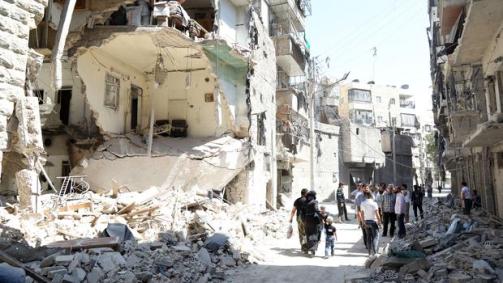 Civillians walk past a damaged building in the war-torn al-Kalasa neighbourhood of the northern Syrian city of Aleppo on July 19, 2015. (Image courtesy of Khaled Khateb/AFP/Getty Images)